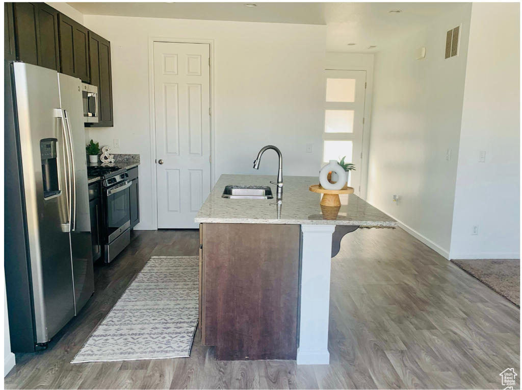 Kitchen featuring a center island with sink, sink, light stone counters, wood-type flooring, and stainless steel appliances