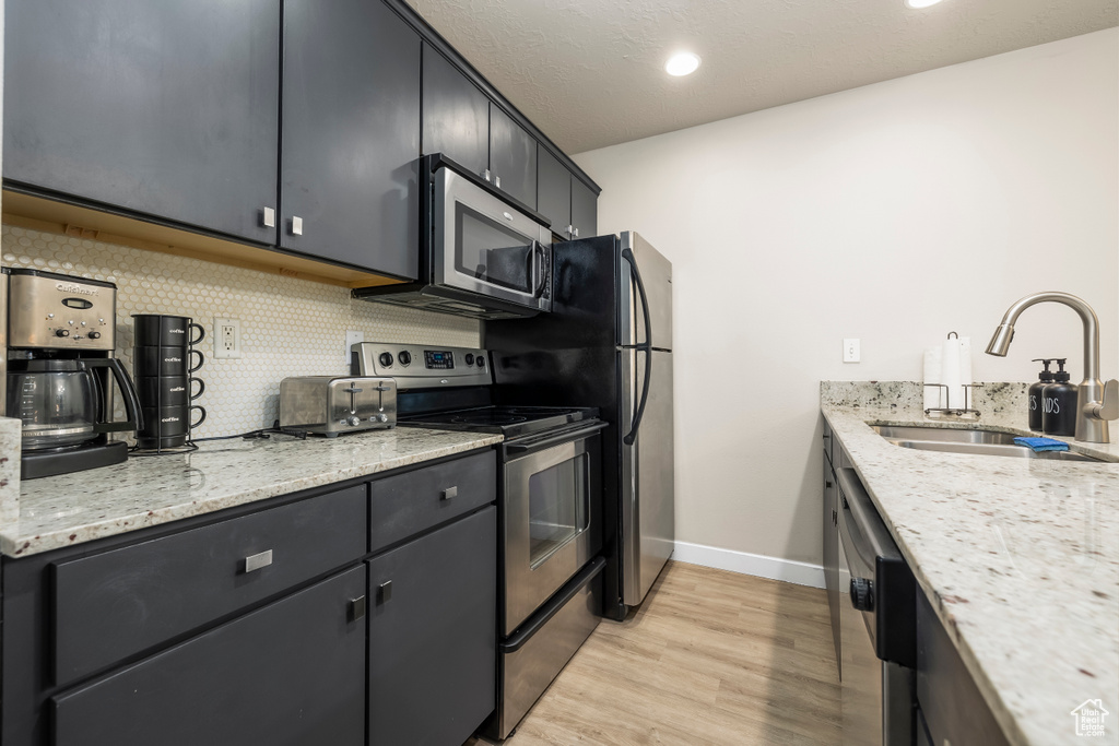 Kitchen featuring light stone countertops, sink, stainless steel appliances, decorative backsplash, and light wood-type flooring