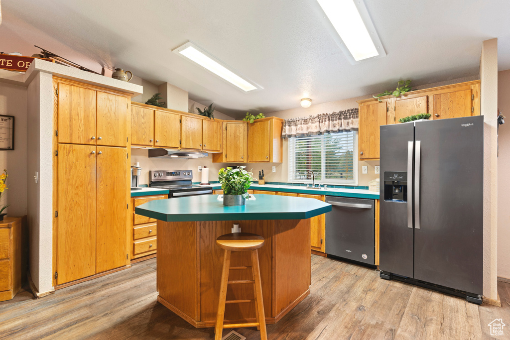 Kitchen with a kitchen bar, appliances with stainless steel finishes, light wood-type flooring, vaulted ceiling, and a kitchen island