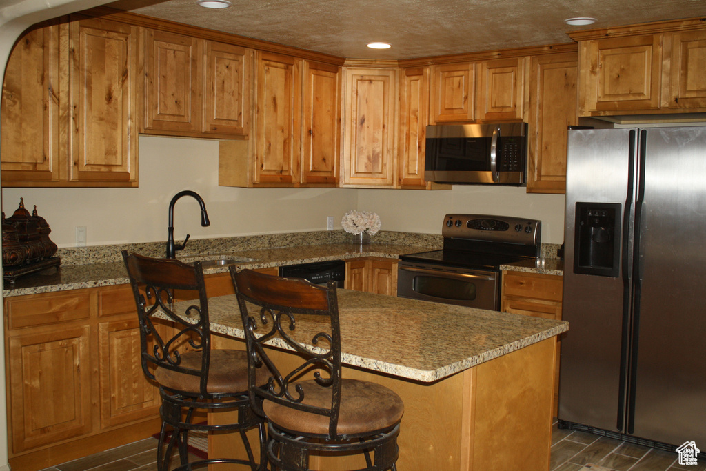 Kitchen with light stone countertops, a kitchen bar, stainless steel appliances, and sink