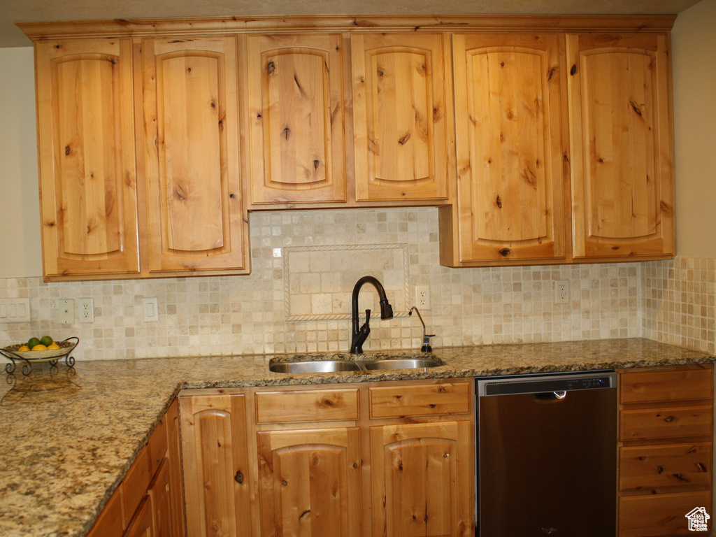 Kitchen featuring light stone countertops, backsplash, stainless steel dishwasher, and sink