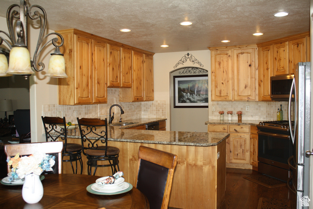 Kitchen with a breakfast bar, dark wood-type flooring, sink, light stone countertops, and appliances with stainless steel finishes