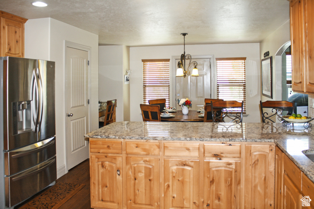 Kitchen with hanging light fixtures, an inviting chandelier, stainless steel fridge with ice dispenser, light stone counters, and dark hardwood / wood-style floors