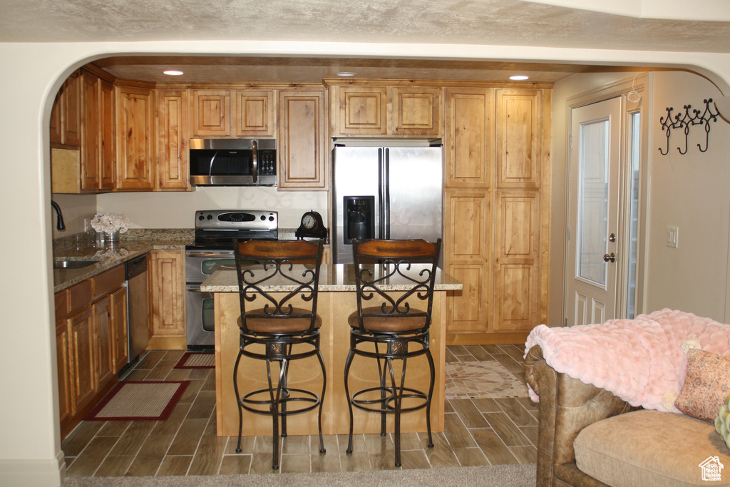 Kitchen with stone counters, a center island, sink, stainless steel appliances, and a breakfast bar area