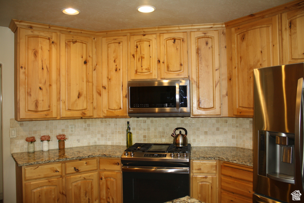 Kitchen with light stone countertops, stainless steel appliances, and tasteful backsplash