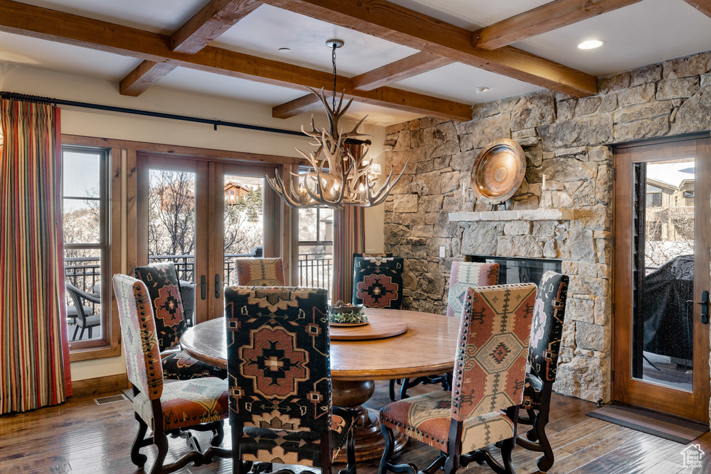 Dining area with a stone fireplace, hardwood / wood-style floors, french doors, and a notable chandelier