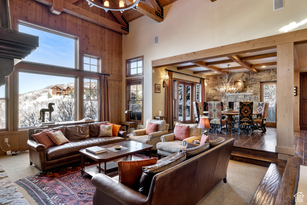 Living room with wooden walls, beam ceiling, a chandelier, a high ceiling, and carpet floors