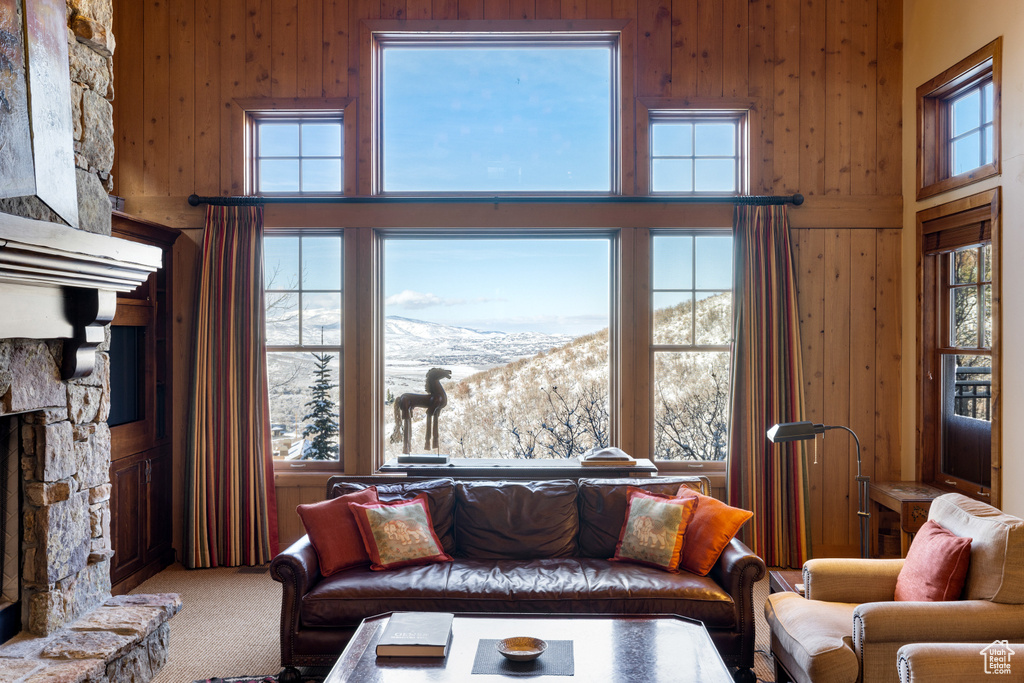 Carpeted living room featuring a mountain view, a stone fireplace, plenty of natural light, and wooden walls