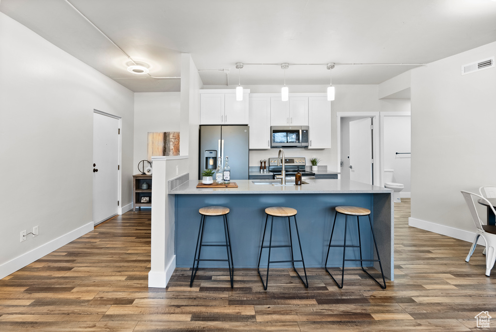 Kitchen with pendant lighting, a kitchen bar, white cabinets, appliances with stainless steel finishes, and dark hardwood / wood-style flooring