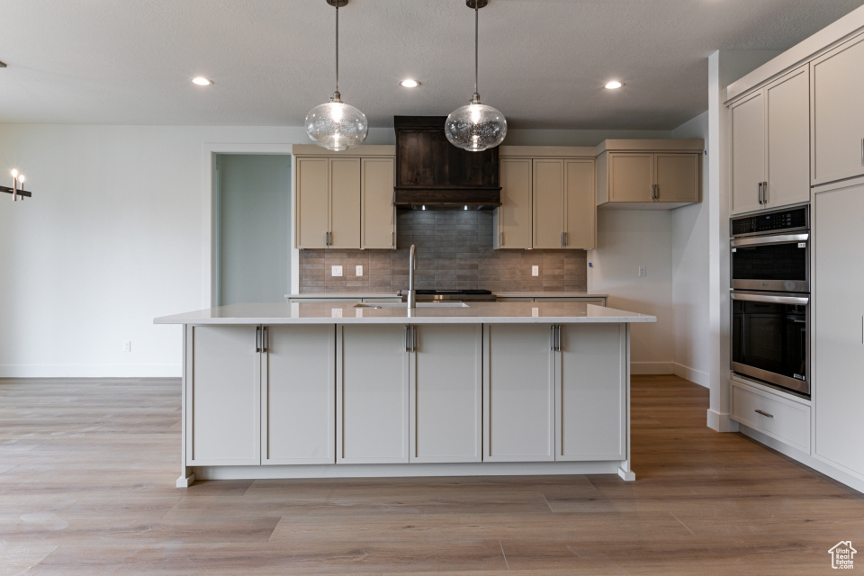 Kitchen featuring double oven, custom range hood, baseboards, and light countertops
