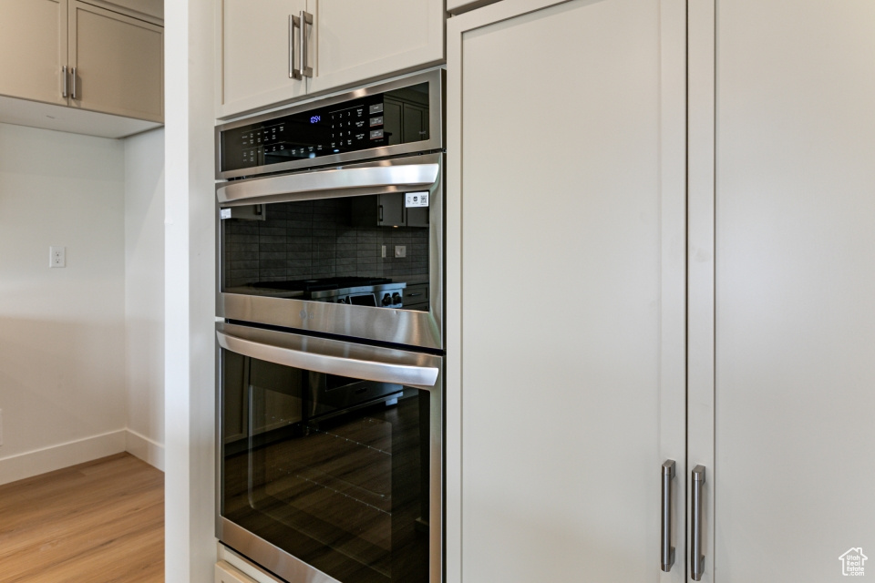 Kitchen with baseboards, decorative backsplash, light wood finished floors, and stainless steel double oven