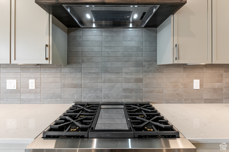 Kitchen with white cabinets, light stone counters, ventilation hood, gas stovetop, and backsplash