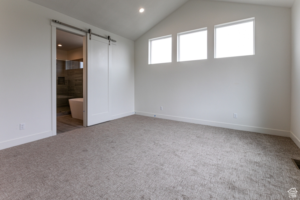 Unfurnished bedroom featuring a barn door, carpet floors, recessed lighting, baseboards, and lofted ceiling