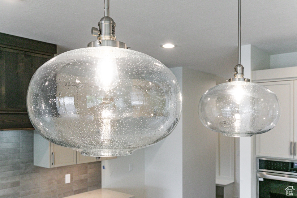 Interior details with stainless steel oven, recessed lighting, decorative light fixtures, white cabinetry, and backsplash