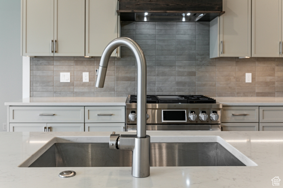 Kitchen featuring under cabinet range hood, backsplash, light stone counters, and gas range