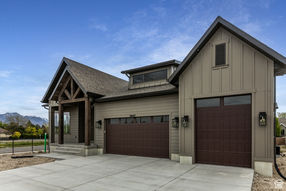 View of front of property with board and batten siding, driveway, roof with shingles, a mountain view, and an attached garage