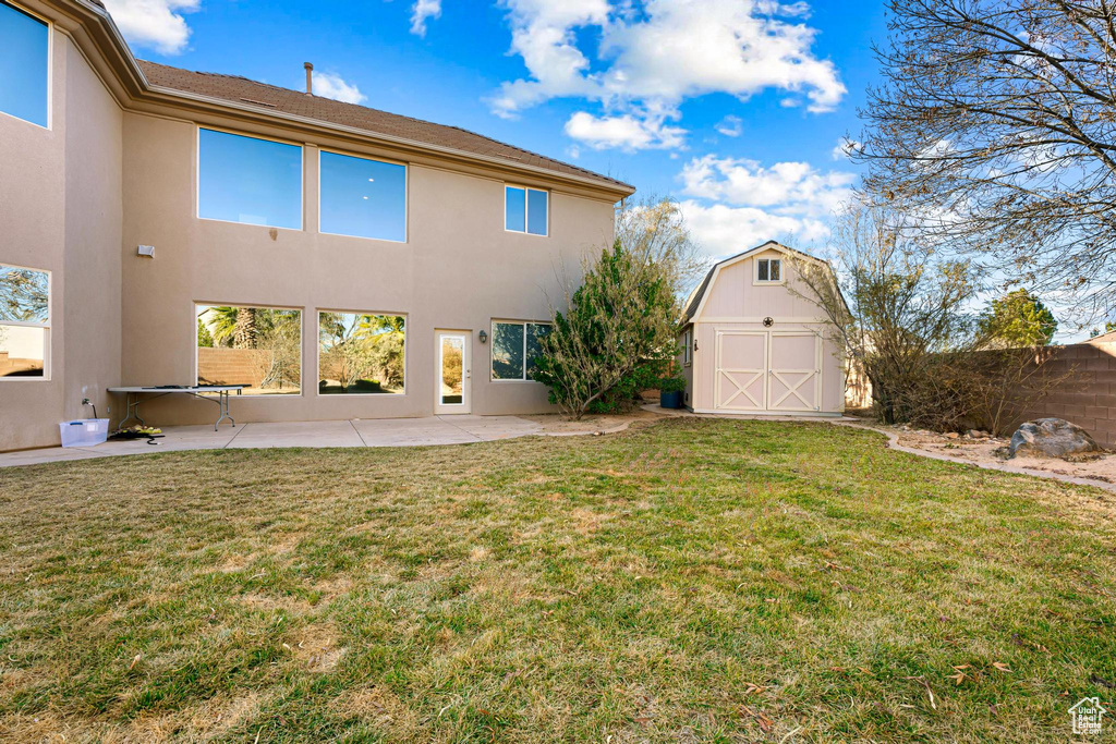 Rear view of property featuring a lawn, a storage unit, and a patio