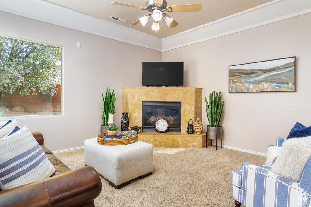 Carpeted living room with a tiled fireplace, ceiling fan, and ornamental molding