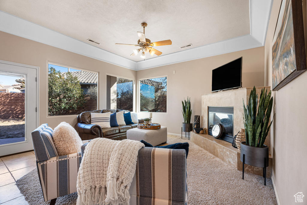 Tiled living room featuring a raised ceiling, ceiling fan, and a premium fireplace