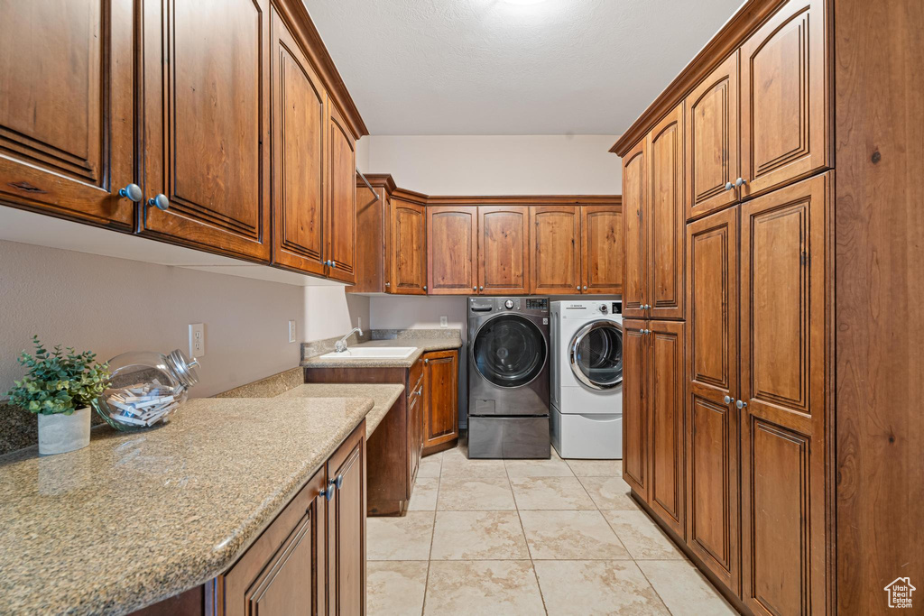 Laundry area featuring washing machine and dryer, sink, light tile patterned floors, and cabinets
