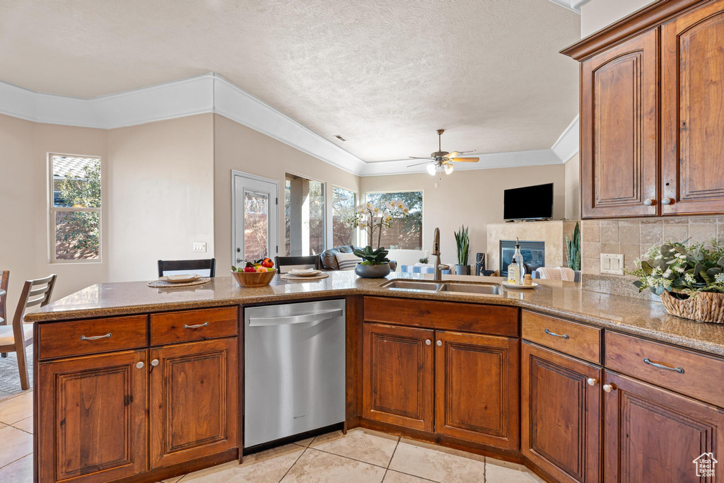 Kitchen featuring ceiling fan, sink, stainless steel dishwasher, a fireplace, and light tile patterned floors