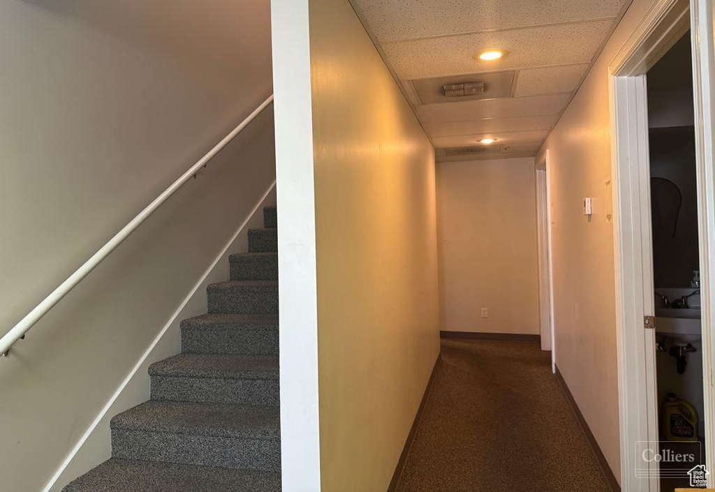 Corridor with a paneled ceiling and dark colored carpet