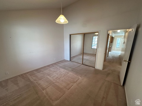 Unfurnished bedroom with a closet, light colored carpet, and vaulted ceiling
