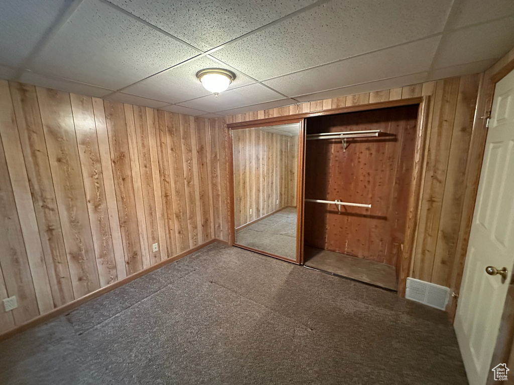 Unfurnished bedroom featuring a paneled ceiling, wood walls, light carpet, and a closet