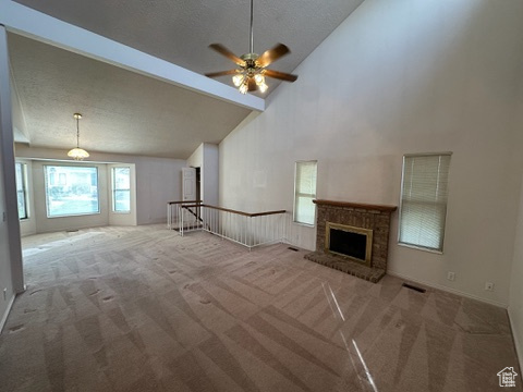 Unfurnished living room featuring carpet, high vaulted ceiling, ceiling fan, a fireplace, and beam ceiling
