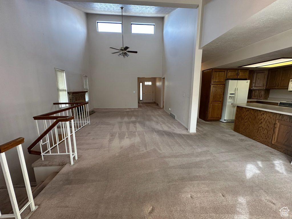 Unfurnished living room with a textured ceiling, ceiling fan, light carpet, and a high ceiling