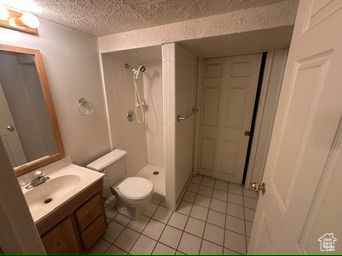 Bathroom with tile patterned flooring, a shower, a textured ceiling, toilet, and vanity