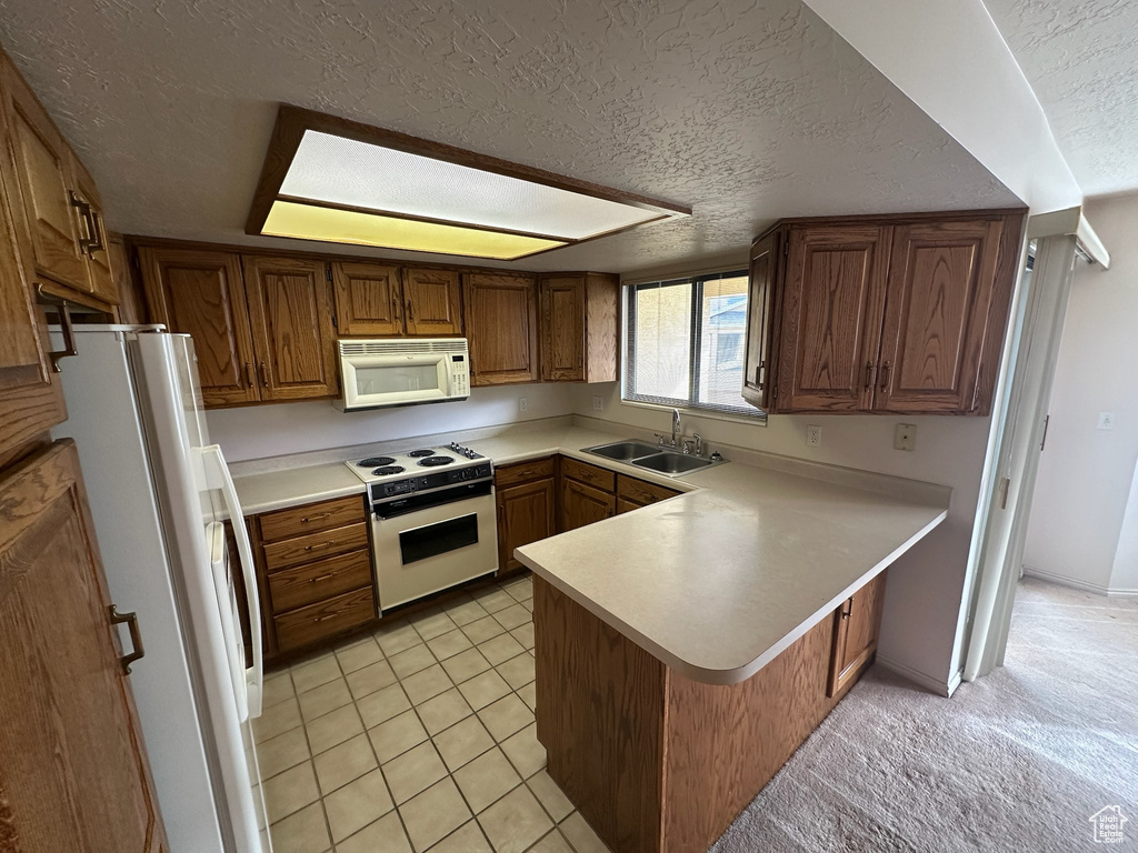 Kitchen with white appliances, sink, a textured ceiling, light tile patterned flooring, and kitchen peninsula
