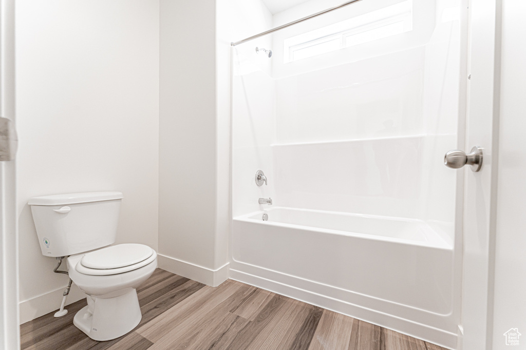 Full bathroom with baseboards, wood finished floors, toilet, and shower / bath combination