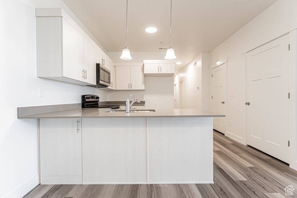 Kitchen with appliances with stainless steel finishes, a peninsula, a sink, light countertops, and light wood-style floors