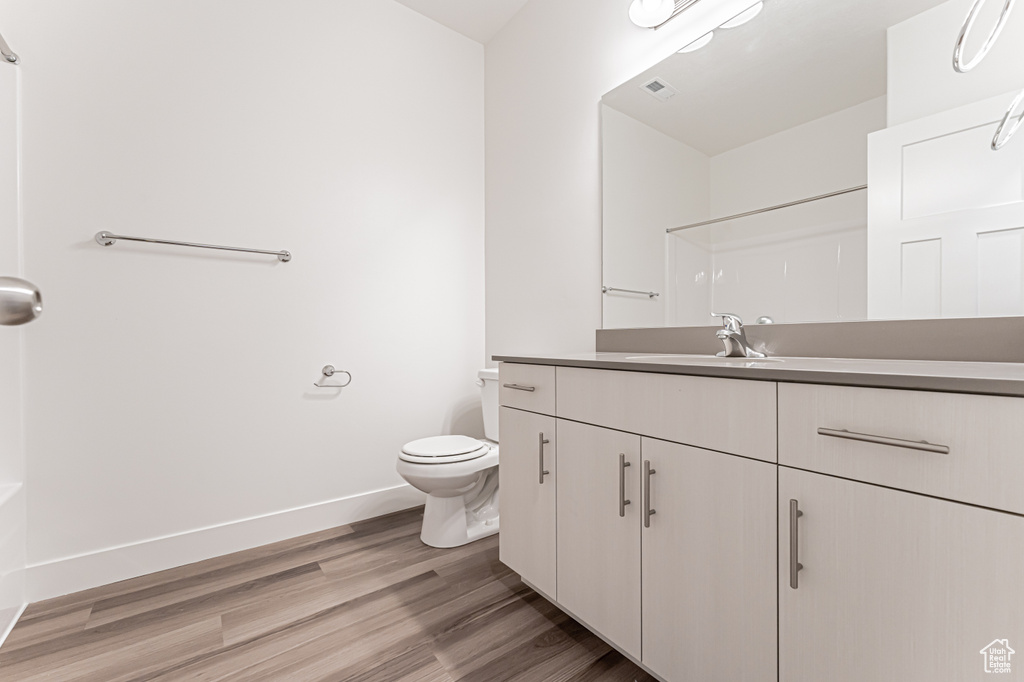 Full bath featuring vanity, wood finished floors, toilet, baseboards, and a shower