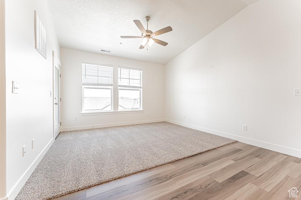 Unfurnished room featuring light wood-style flooring, ceiling fan, vaulted ceiling, baseboards, and a textured ceiling