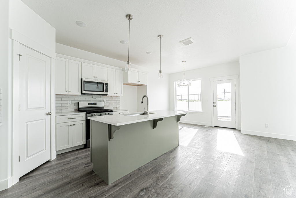 Kitchen featuring appliances with stainless steel finishes, a sink, wood finished floors, a breakfast bar, and a kitchen island with sink