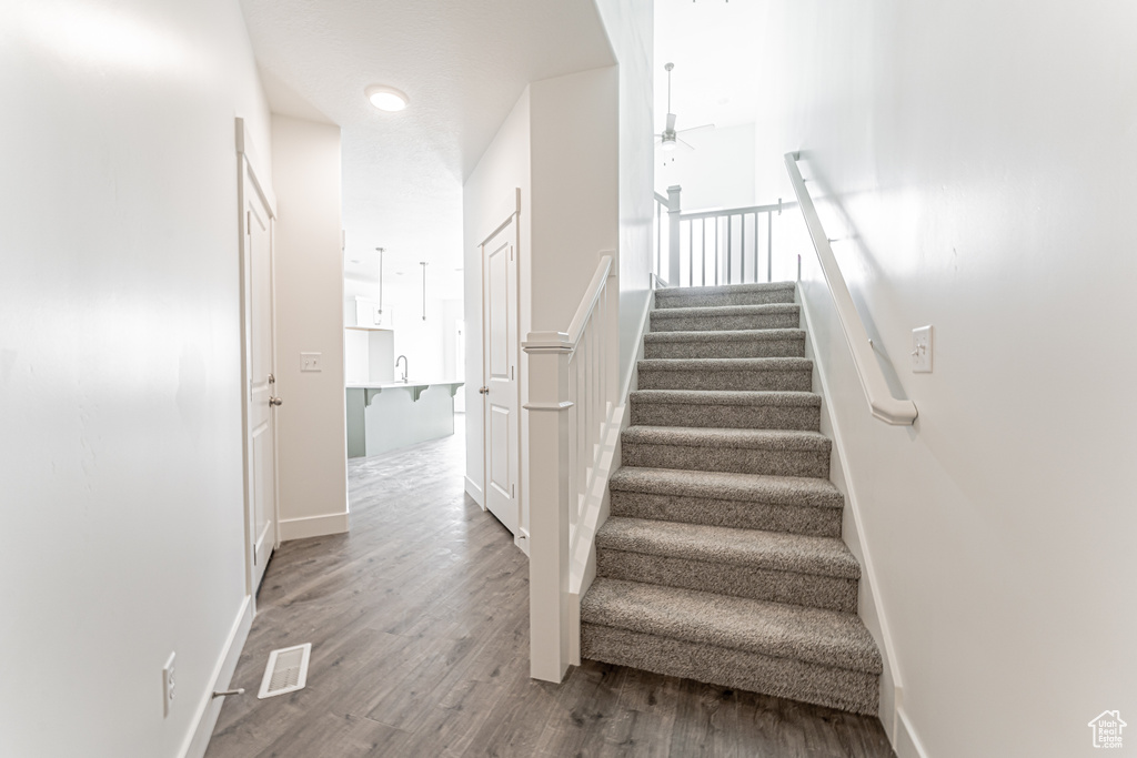 Stairway with ceiling fan, wood finished floors, and baseboards