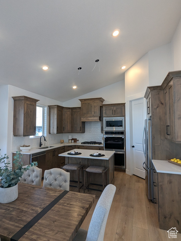 Kitchen with sink, stainless steel appliances, backsplash, vaulted ceiling, and a kitchen island