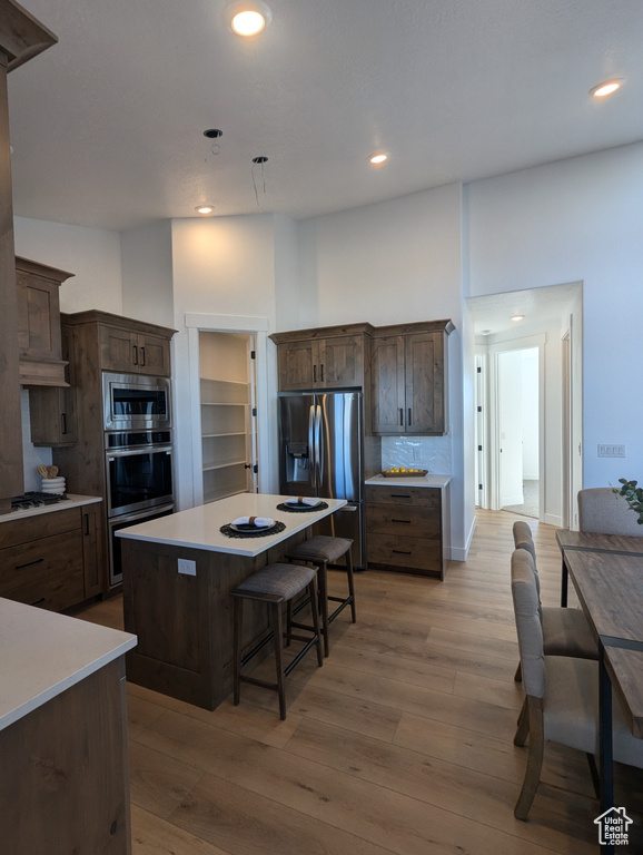 Kitchen featuring a kitchen bar, appliances with stainless steel finishes, dark brown cabinetry, light hardwood / wood-style flooring, and a kitchen island