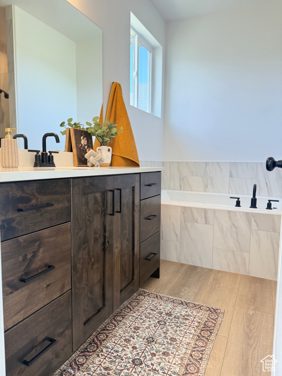 Full bath with vanity, a garden tub, and wood finished floors