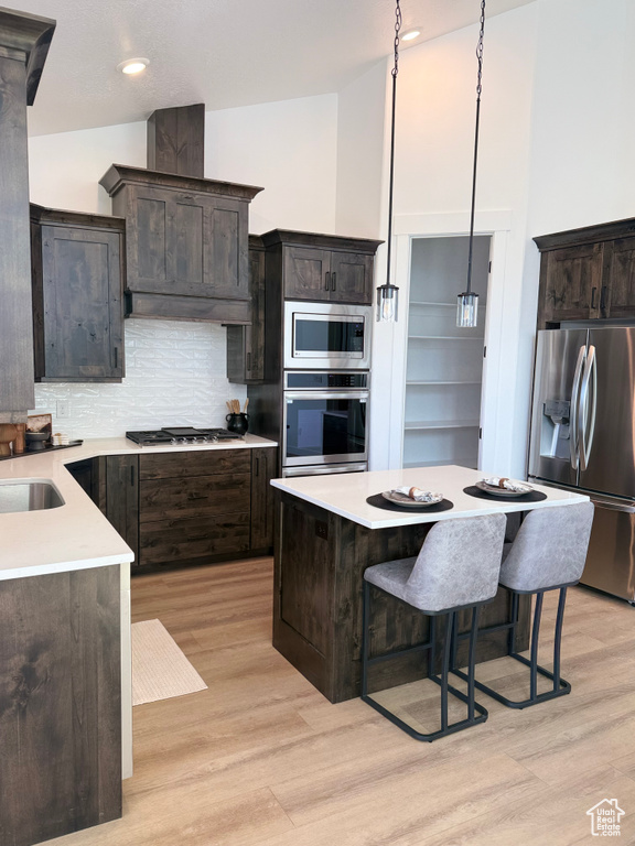 Kitchen with light wood-type flooring, light countertops, appliances with stainless steel finishes, and a kitchen breakfast bar