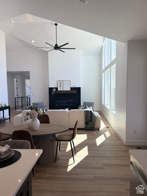 Living room with wood finished floors, baseboards, ceiling fan, high vaulted ceiling, and recessed lighting