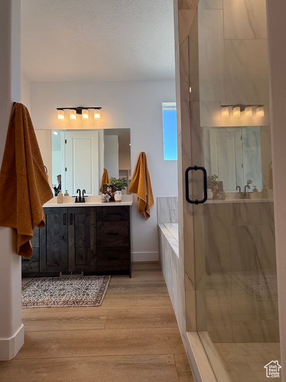 Bathroom featuring a bath, a stall shower, wood finished floors, vanity, and baseboards