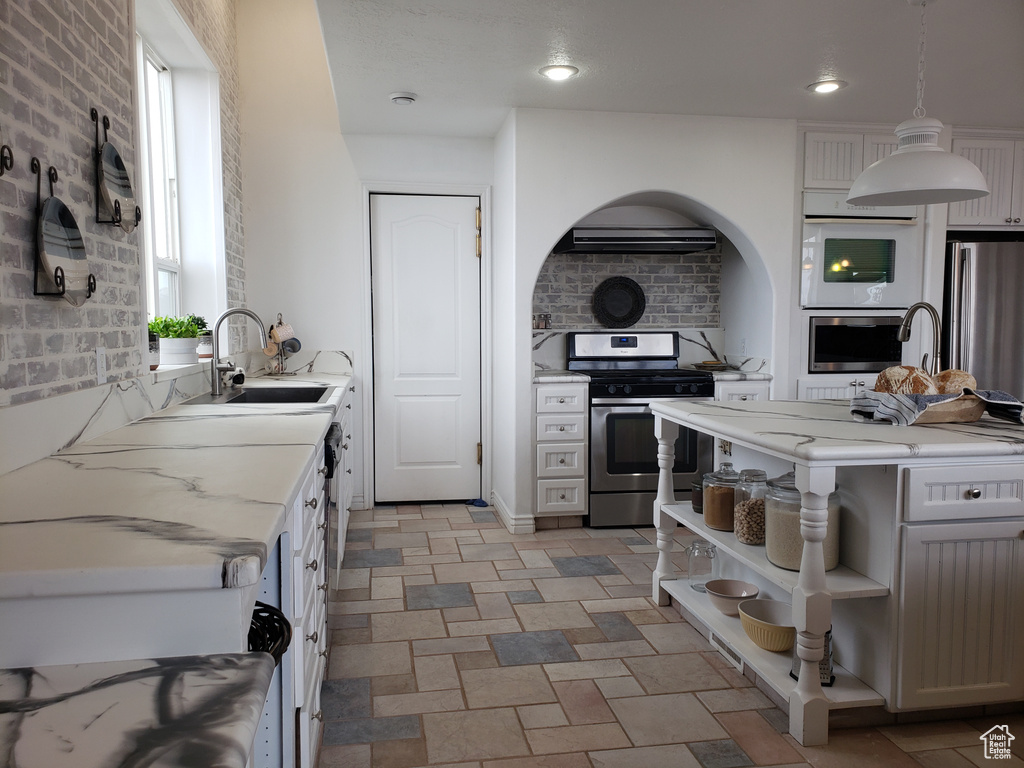 Kitchen featuring sink, hanging light fixtures, a wealth of natural light, white cabinetry, and stainless steel appliances