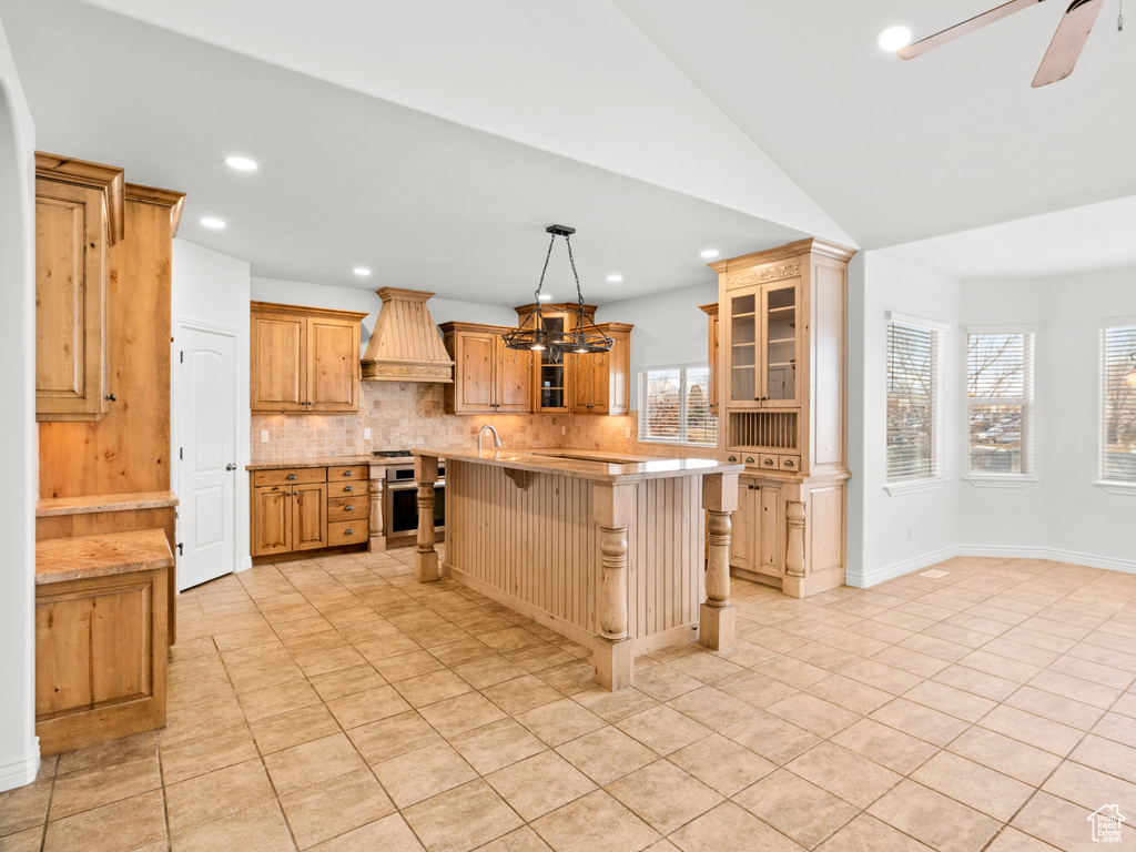 Kitchen with a center island, backsplash, premium range hood, ceiling fan, and a breakfast bar area