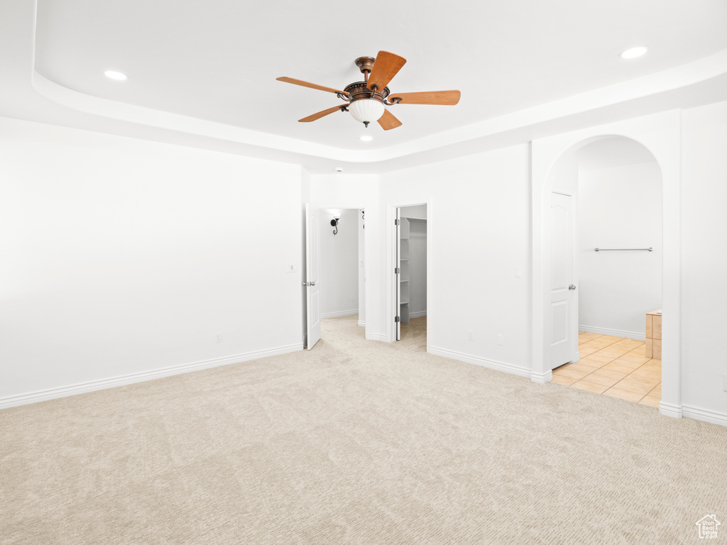 Unfurnished bedroom featuring light carpet, ensuite bath, a tray ceiling, ceiling fan, and a spacious closet