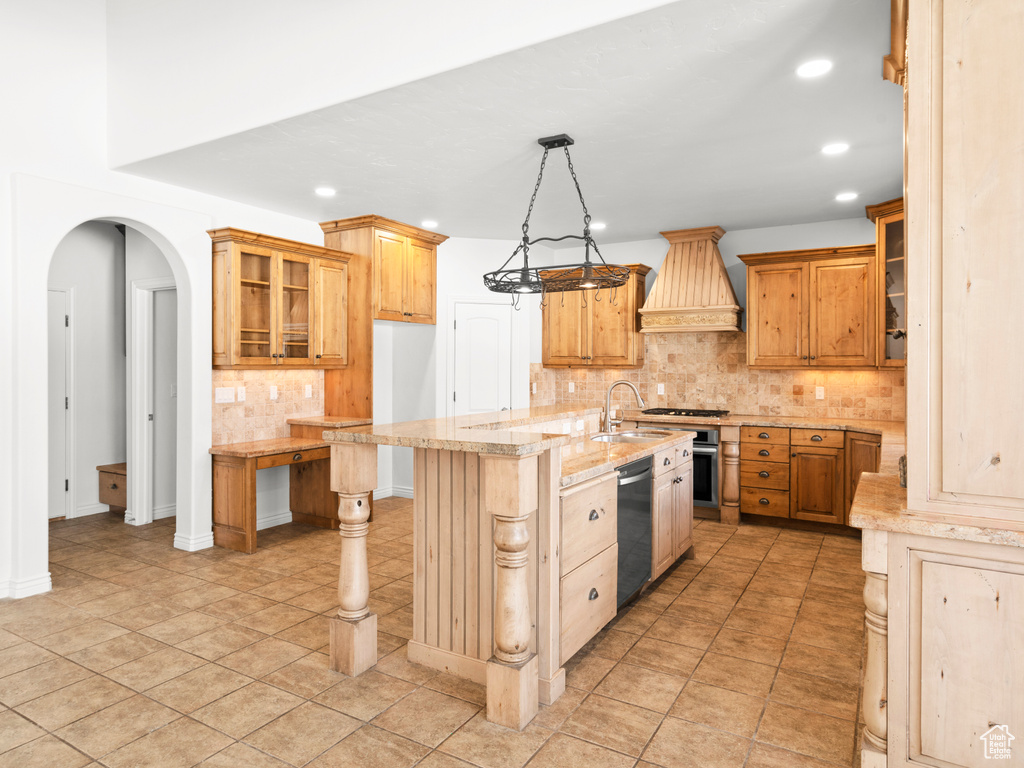 Kitchen featuring appliances with stainless steel finishes, custom range hood, sink, decorative light fixtures, and a center island with sink