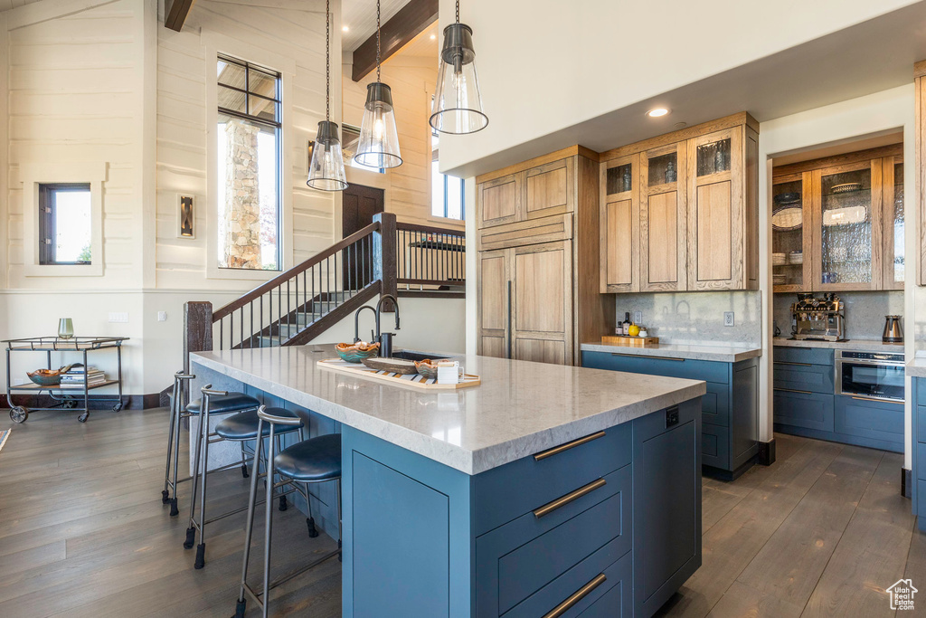 Kitchen featuring beamed ceiling, decorative light fixtures, a kitchen island with sink, and paneled built in fridge