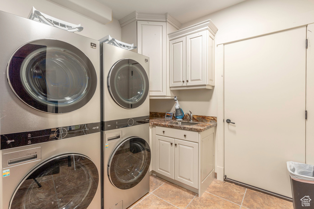 Clothes washing area featuring cabinets, stacked washer and dryer, and sink